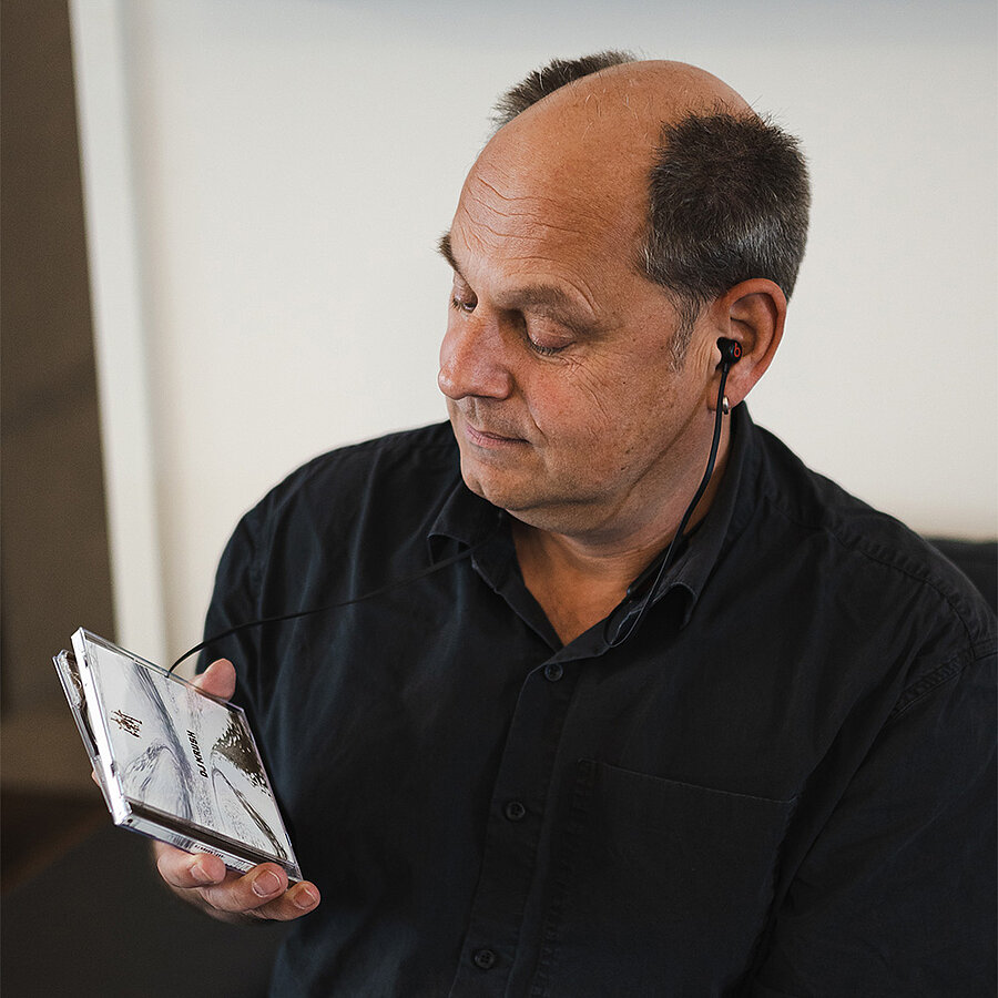 Andreas, Senior SEO-Manager bei der B2B Digitalagentur digit.ly in Hannover, schaut mit Kopfhörern in den Ohren auf ein CD-Cover.