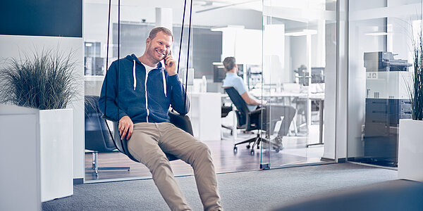 Roland Gaedecke | digit.ly gmbh Mitarbeiter einer B2B Digitalagentur sitzt auf einer Schaukel in der Lounge der Agentur.