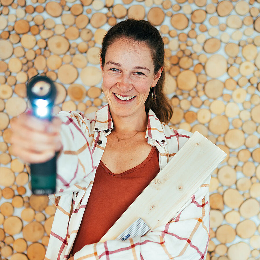 Swantje, Content Marketing Managerin und Head of Operations bei der B2B Digitalagentur digit.ly in Hannover, hält Holz und Zollstock im Arm und eine Bohrmaschine in die Kamera.