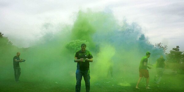 Mitarbeiter von digit.ly stehen in buntem Farbrauch beim Paintball-Teamevent.