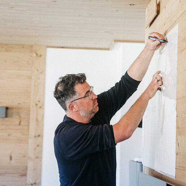 Der Geschäftsführer der Agentur für Webentwicklung digit.ly zeichnet während eines Workshops zur Customer Experience etwas an eine Wand.