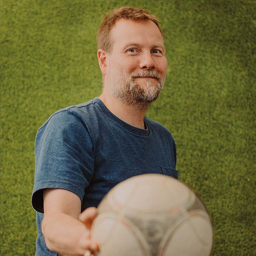 Christian, Projektmanager bei der B2B Digitalagentur digit.ly in Hannover, hält einen Fußball in die Kamera.
