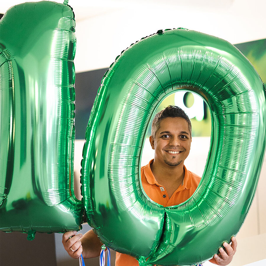 Markus, TYPO3-Entwickler bei der digit.ly B2B Digitalagentur aus Hannover hält die Zahl 10 als grüne Heliumballons hoch.