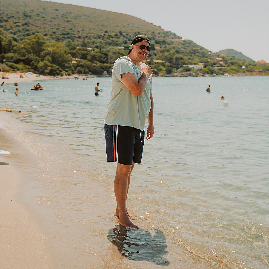 Philip, ehemaliger Geschäftsführer der B2B Digitalagentur digit.ly in Hannover, steht in Badehose und T-Shirt am Strand.