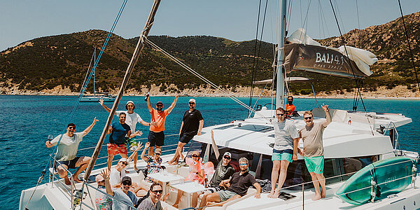 Mitarbeitende winken vom Deck eines Segelschiffs während eines Segelausflugs mit dem Team einer Agentur für Digitales.