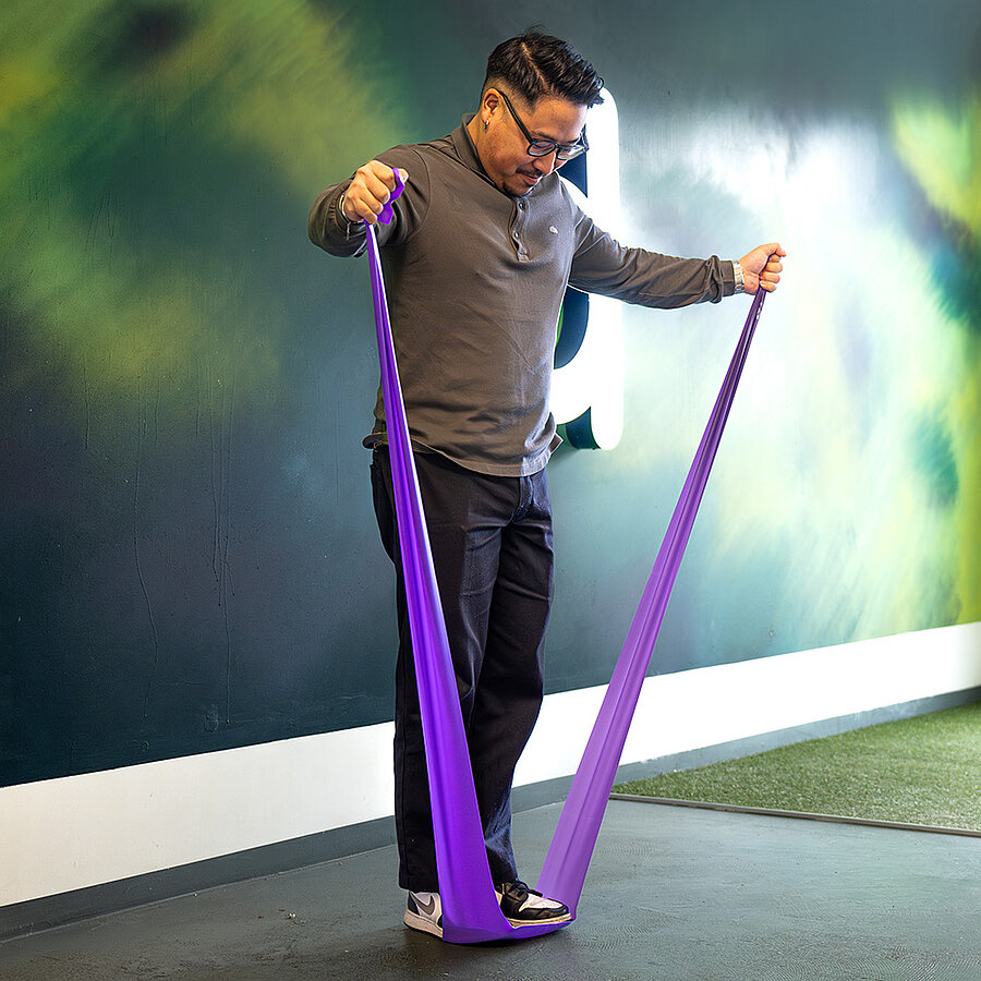 Vu, Digitalberater bei der B2B Digitalagentur digit.ly in Hannover, macht eine Übung mit einem Stretchingband.